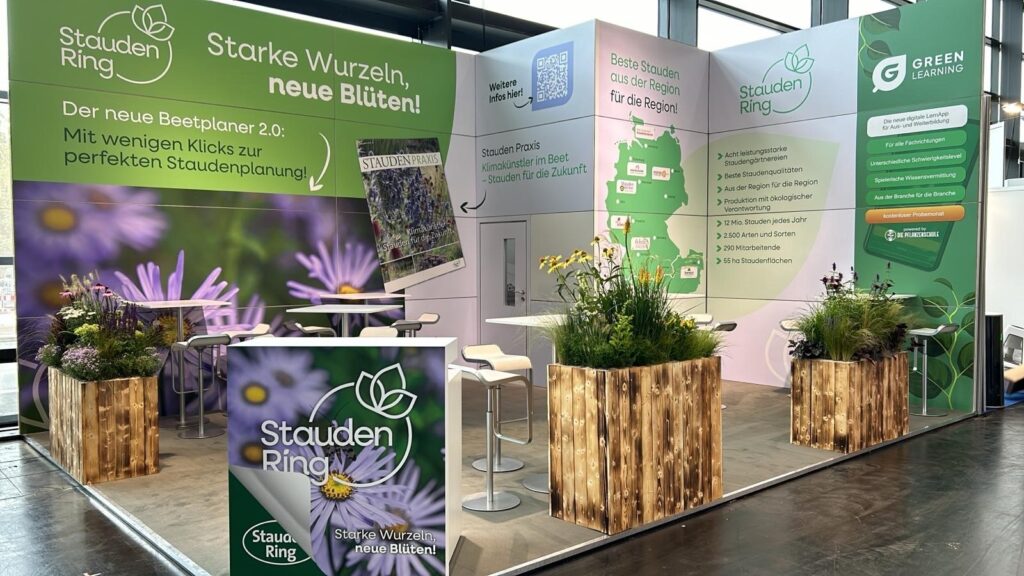 Messestand mit Infotafeln zu Stauden Ring und Green Learning, dekoriert mit Holzkästen voller Staudenpflanzen.