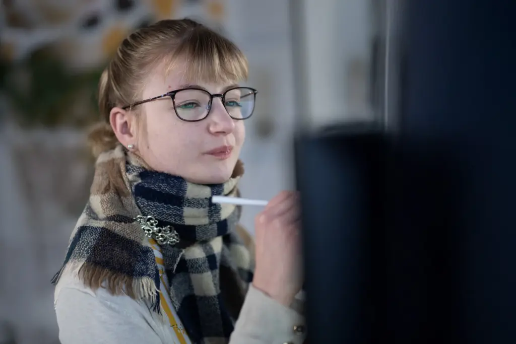 Junge Frau mit Brille und kariertem Schal schreibt mit weißem Stift auf eine vertikale schwarze Fläche.