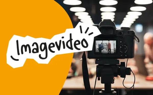 Digitalkamera auf einem Stativ filmt zwei Personen in einem hellen Raum mit vielen Deckenleuchten, davor orangefarbener Bereich mit Schriftzug Imagevideo.